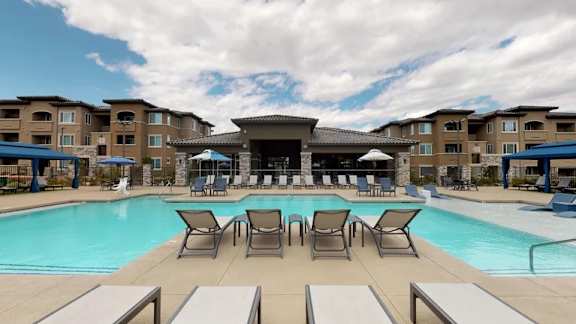 A swimming pool surrounded by lounge chairs and umbrellas in front of apartment buildings.