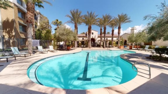 A swimming pool surrounded by lounge chairs and umbrellas in front of apartment buildings.