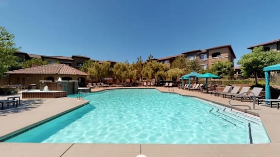 a large swimming pool with chairs and a building in the background