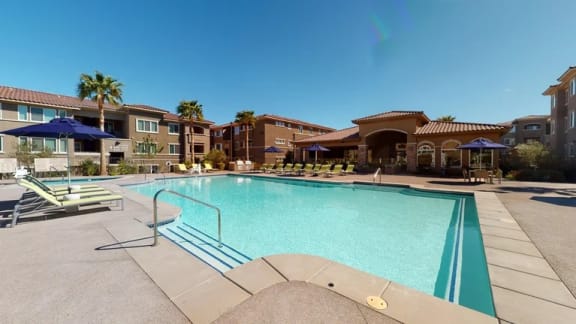 A swimming pool surrounded by lounge chairs and umbrellas in front of apartment buildings.