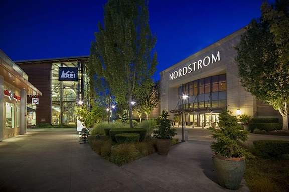 A Nordstrom store is lit up at night with a clear blue sky in the background.