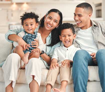 A family of four is sitting on a couch together.