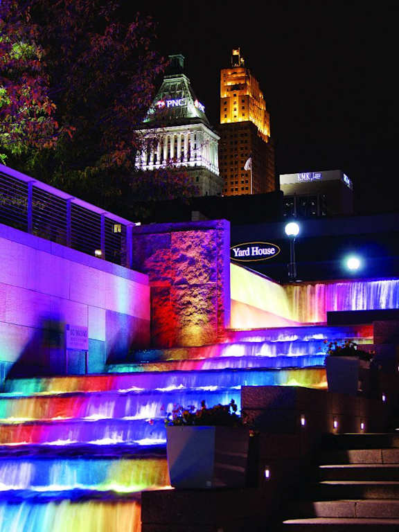 A colorful light display at a waterfall in front of a building.at Sky Central, Cincinnati Ohio