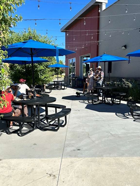 A group of people are sitting at tables under blue umbrellas in a courtyard.