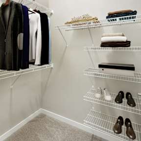 A white closet with clothes and shoes on shelves.