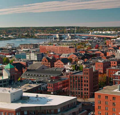 A cityscape with buildings in the foreground and a body of water in the background.