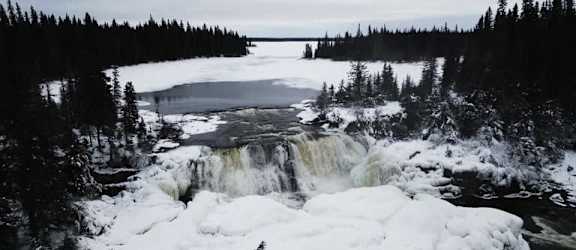 a waterfall in the snow next to a frozen lake