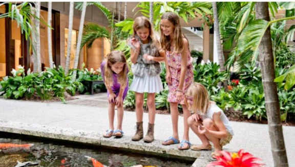 Four children are standing on a stone platform by a pond.