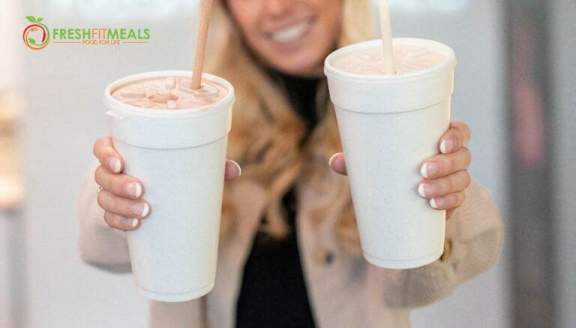 A woman holding two cups of a chocolate-colored beverage.