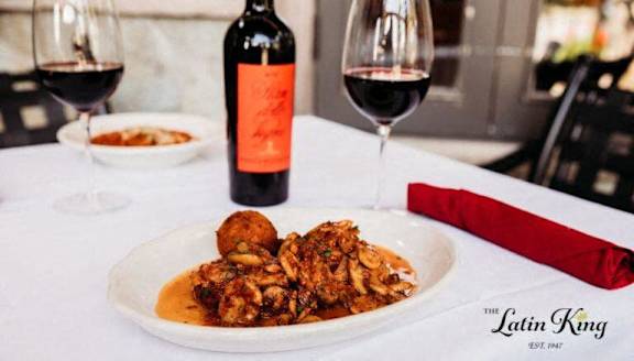 A bottle of red wine is on a table next to two glasses of wine and a plate of food.