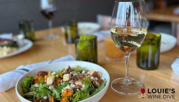 A table with a bowl of salad and glasses of white wine.