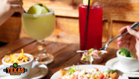 A person is eating a salad at a table with a glass of lemonade and a candle in the background.