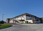 Thumbnail 1 of 12 - The Parq is a large, modern building with a parking lot in front.