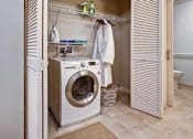Thumbnail 12 of 12 - A white washing machine is in a small laundry room.