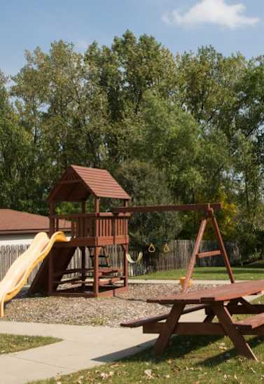 A wooden play structure with a yellow slide and a picnic table.