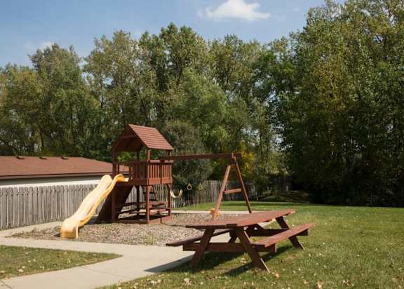 A wooden play structure with a yellow slide and a picnic table.