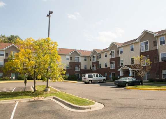 A parking lot in front of apartment buildings with a tree in the foreground.