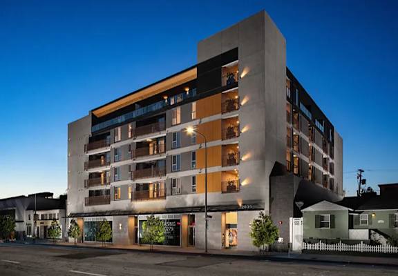 A modern building with a mix of beige and brown balconies is illuminated at dusk.