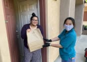 Thumbnail 1 of 13 - A Mutual Housing staff person hands a resident a grocery bag in her doorway