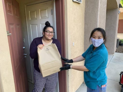 A mutual housing staff member hands a grocery bad to a resident in her doorway