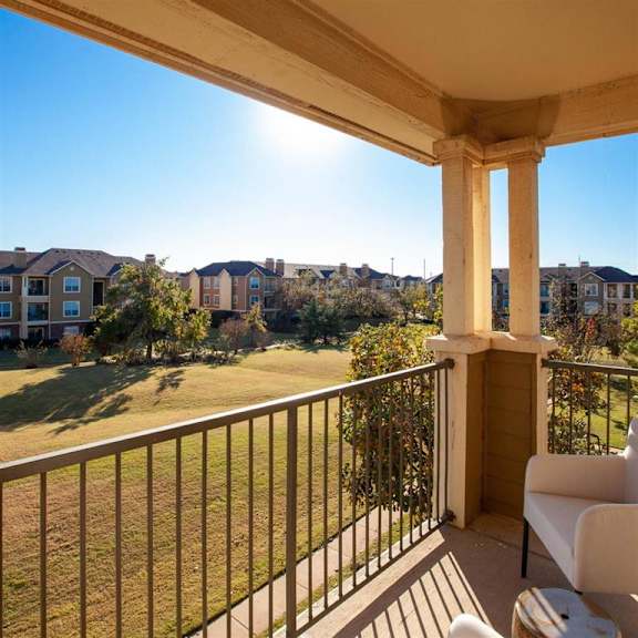 A concrete and metal balcony with a gorgeous view of the rolling grassy field with trees at Sycamore Farms Apartment Homes. 