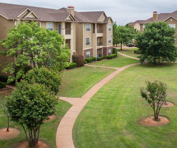 The large, grassy area with a pathway and trees behind the apartment buildings at Sycamore Farms Apartment Homes. 