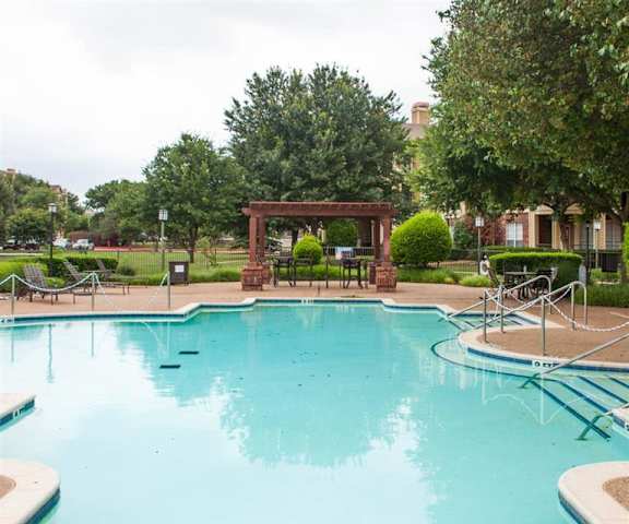 Sycamore Farms Pool The large, turquoise outdoor pool with pool chairs with greenery, trees, and the apartments in the background at Sycamore Farms Apartments.