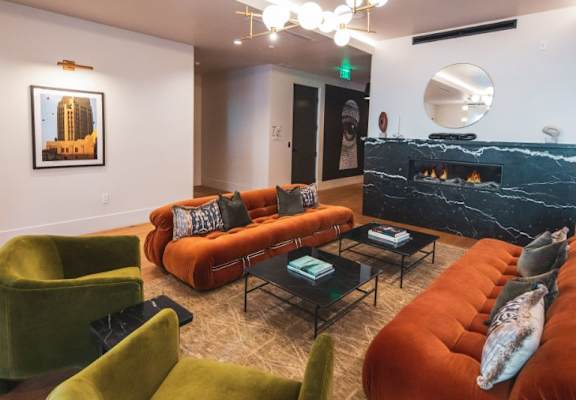 Living room with orange couches and green chairs and a fireplace at Fedora x Trilby in Los Angeles, CA 90005