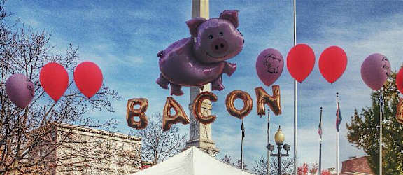 a group of people standing in front of a pig roast sign