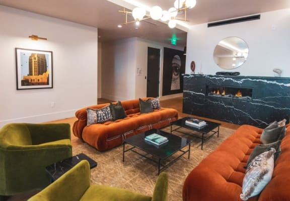 Living room with orange couches and green chairs and a fireplace at Fedora x Trilby in Los Angeles, CA 90005
