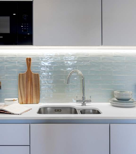 A kitchen with a white sink and a wooden cutting board.