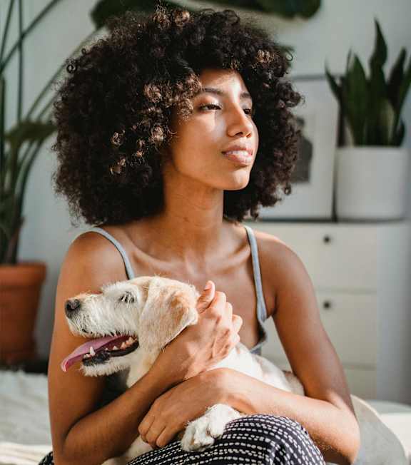 A woman with curly hair is holding a small dog.