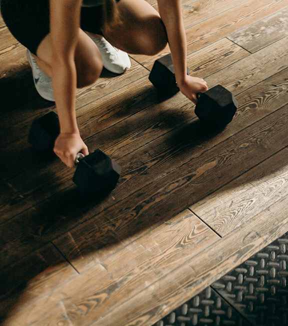A person is lifting weights on a wooden floor.