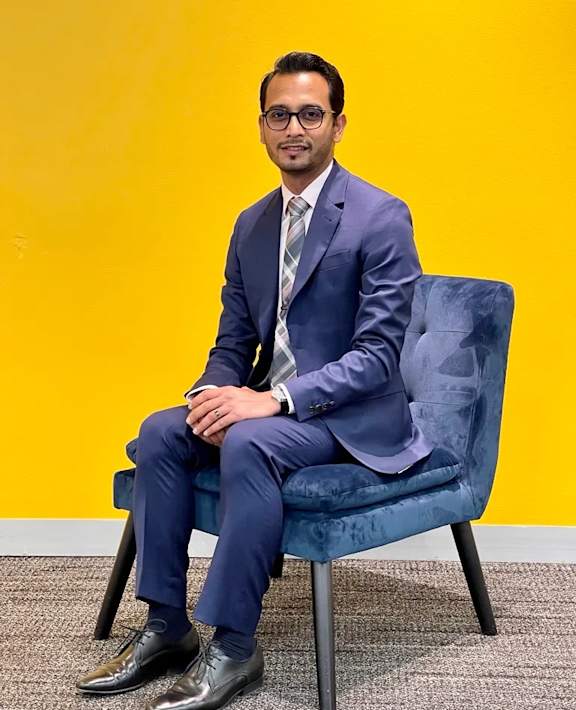 A man in a suit sits on a blue chair.