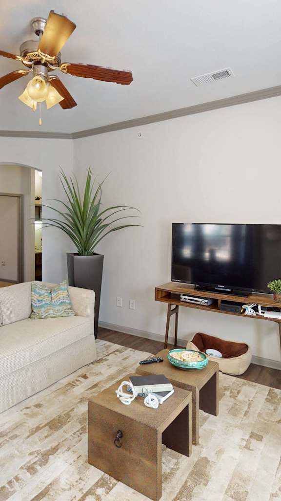 An open apartment layout with a living room ceiling fan, a dining area with bay windows, and a fully-equipped gourmet kitchen.