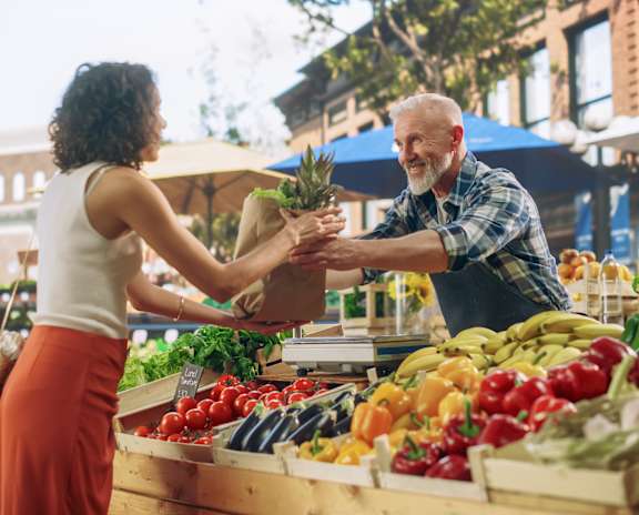A woman is handing a pineapple to a man at a fruit stand.