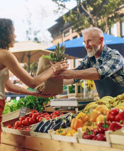 A woman is handing a pineapple to a man at a fruit stand.