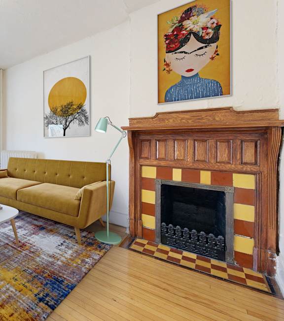 A living room with a yellow couch, a fireplace, and a painting on the wall.