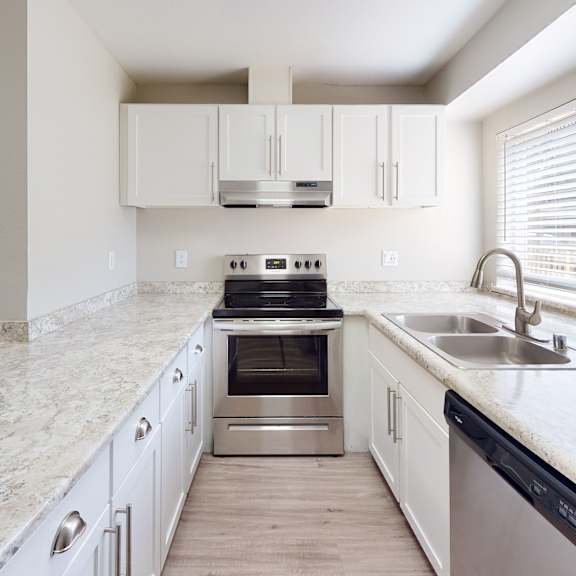 a kitchen with white cabinets and a large window at The Village at Seeley Lake Apartments, Lakewood, WA