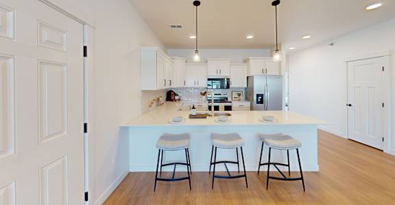 A kitchen with white cabinets and a white island with three bar stools.