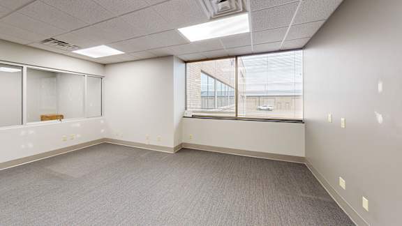 A spacious office room with a window overlooking a parking lot.