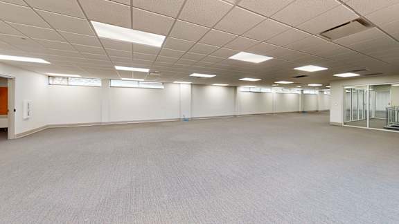 A large, empty room with carpeted flooring and fluorescent lighting.