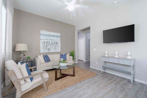 A living room with a white couch, a chair, a coffee table, and a flat screen TV mounted on the wall at Vistoria At Country Place Apartments, Tolleson, Arizona