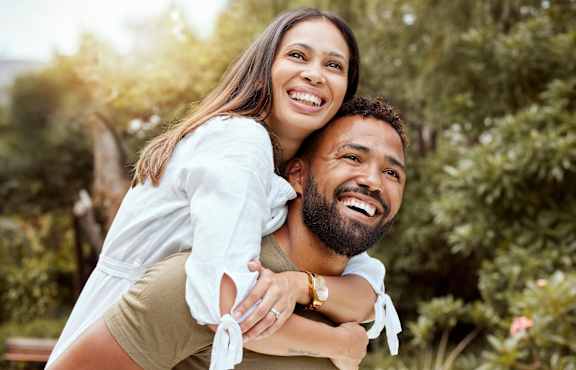 A man is carrying a woman on his back in a park.
