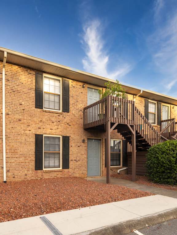 A brick building with a balcony and a car parked in front.