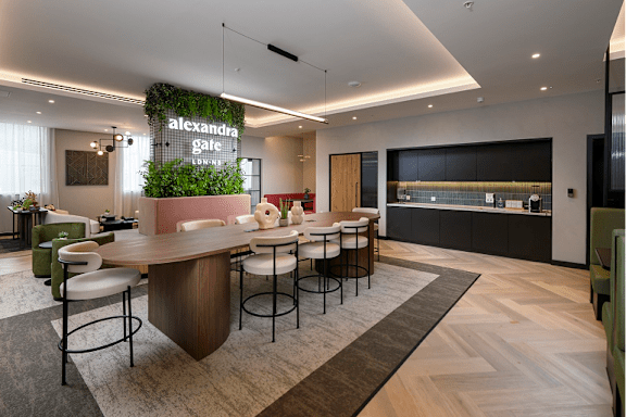 A modern office space with a green plant hanging from the ceiling and a long wooden table with chairs.