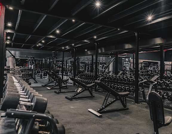 A gym with a variety of equipment including dumbbells, weight plates, and benches.