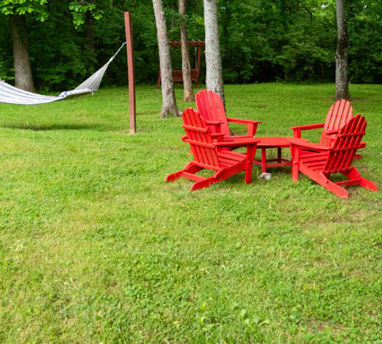 Two red chairs and a table are set up in a grassy area.