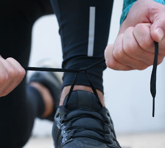 A person is tying the laces of a black shoe.