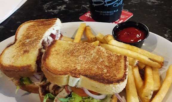 A sandwich and fries are served on a plate with a bottle of B.B.Q. sauce in the background.